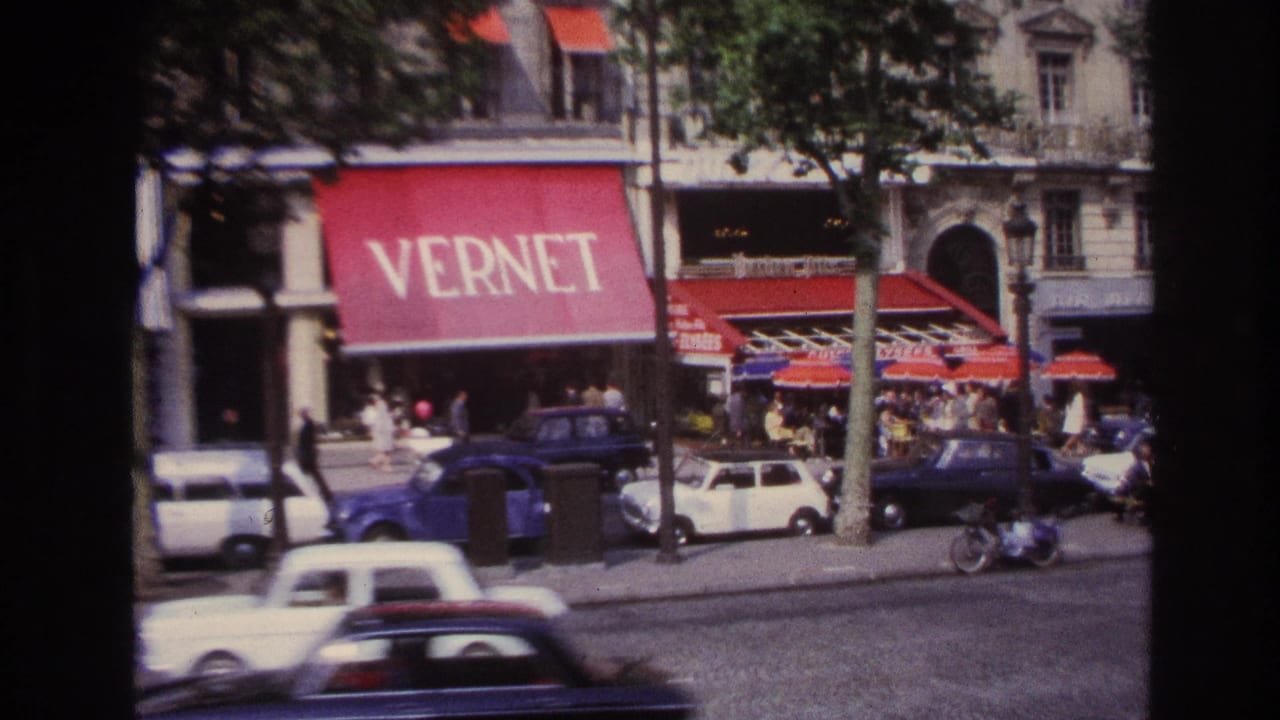 Paris street with red VERNET awning, pedestrians, parked cars, and passing traffic.