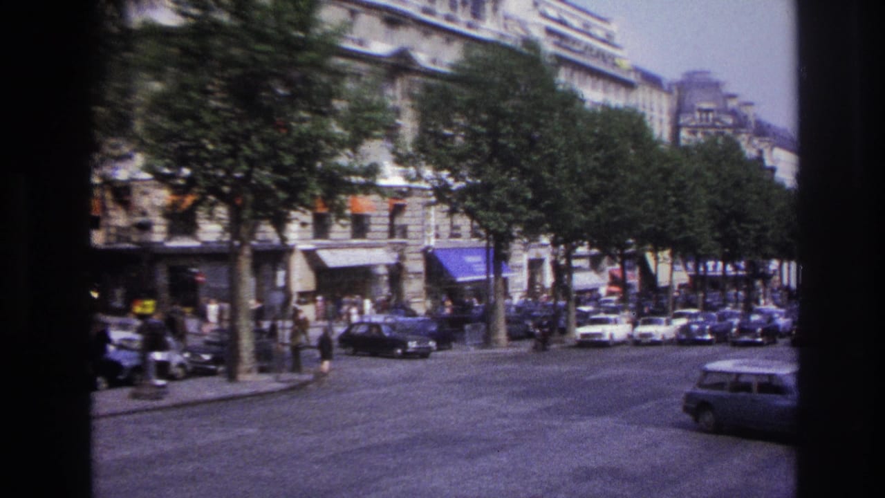 1967 Paris street view from a moving vehicle, showing traffic, pedestrians, trees, awnings, and multi-story stone facades.