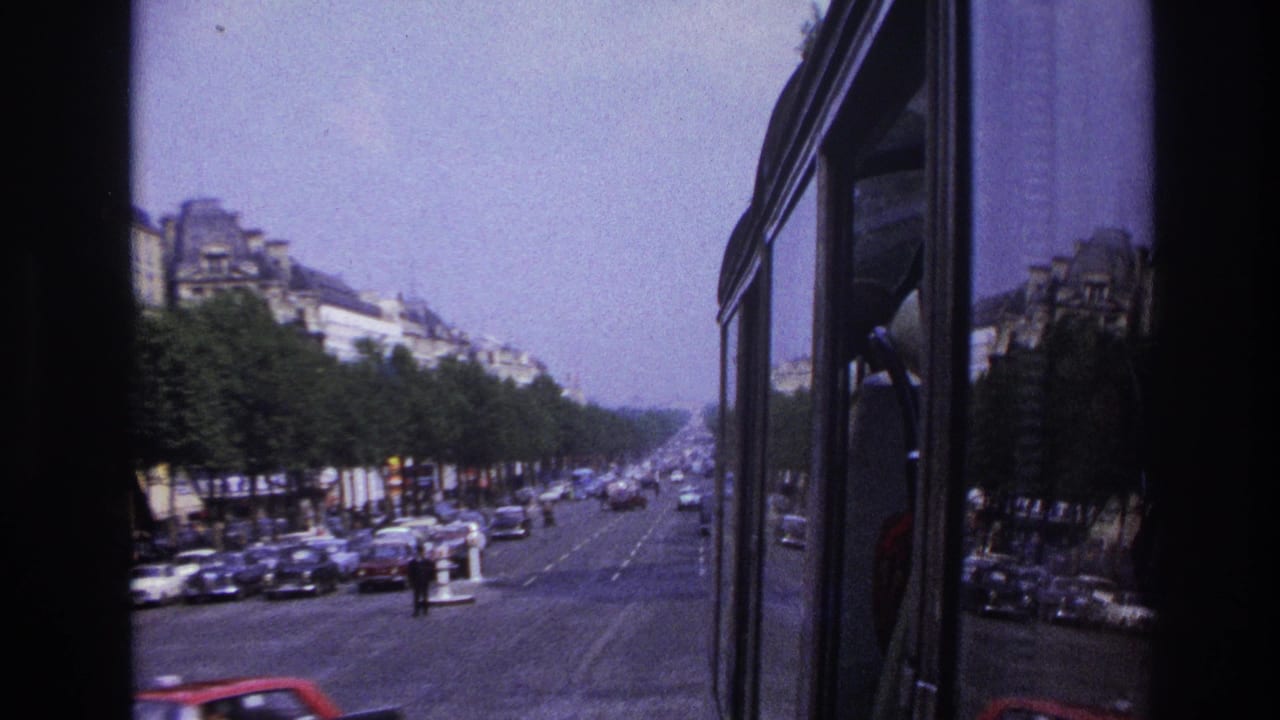 1967 Paris bus-window view down a broad tree-lined boulevard with mid-century cars, pedestrians, and multi-story buildings.
