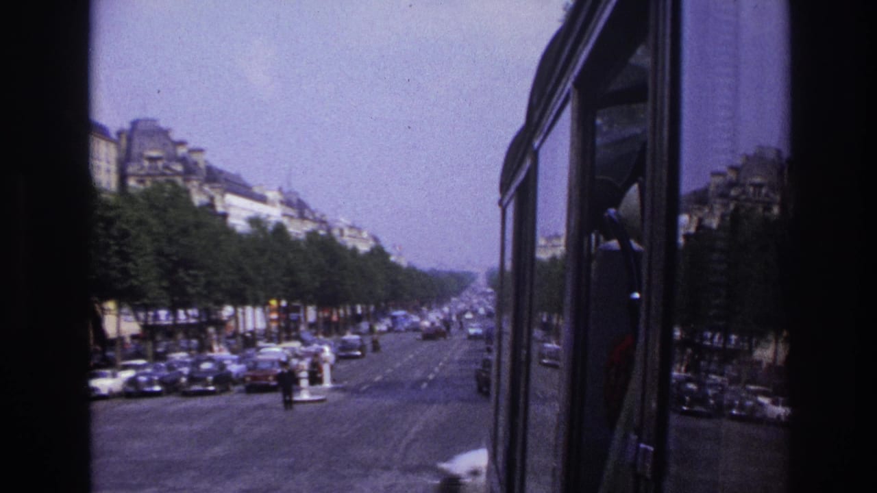 1967 Paris street scene from a bus, showing the vehicle side, boulevard traffic, rows of trees, and distant apartment buildings.