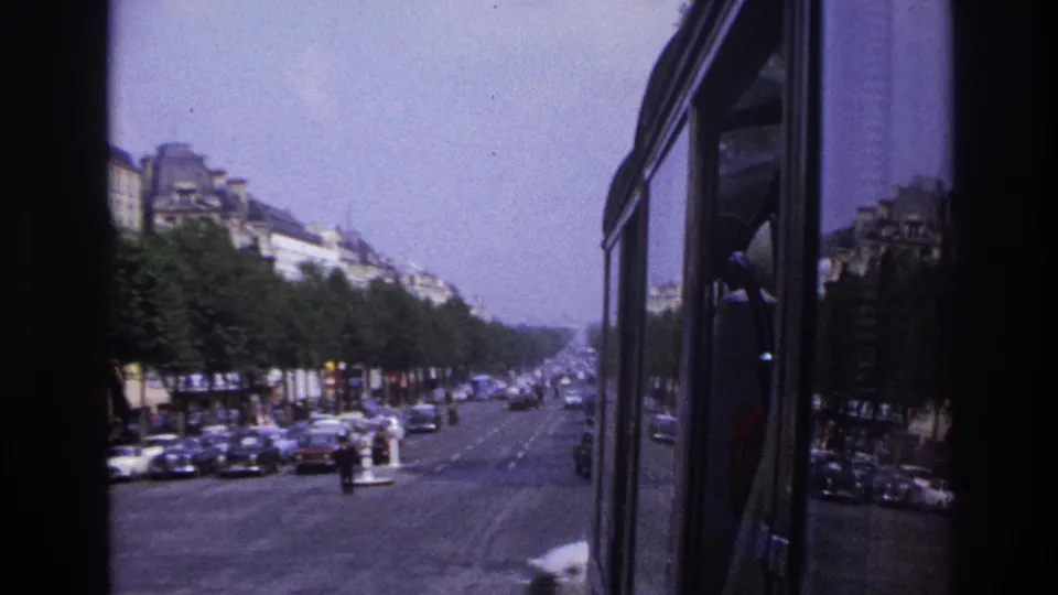 1967 Paris street scene from a bus, showing the vehicle side, boulevard traffic, rows of trees, and distant apartment buildings.