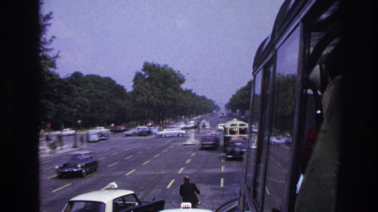 Cars and a bus move along a wide boulevard framed by vehicle windows.