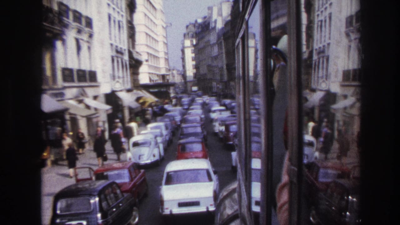 Cars line the roadway while pedestrians move along sidewalks beside awning-covered storefronts.