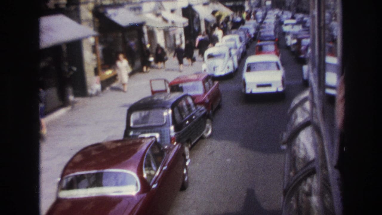 1967 Paris street view from above or a moving vehicle, showing dense traffic, parked cars, shopfronts, and pedestrians along the sidewalk.