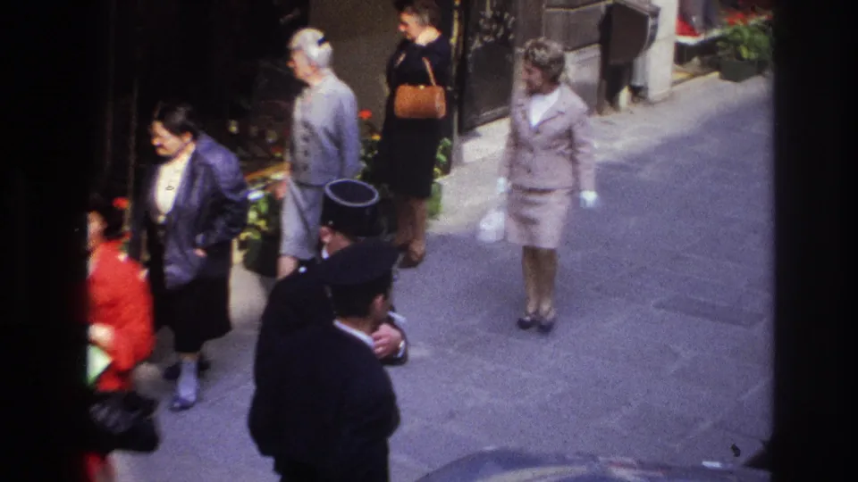 Closer 1967 Paris sidewalk view with several adults passing a storefront, including a woman in red, formally dressed women, and a uniformed man.