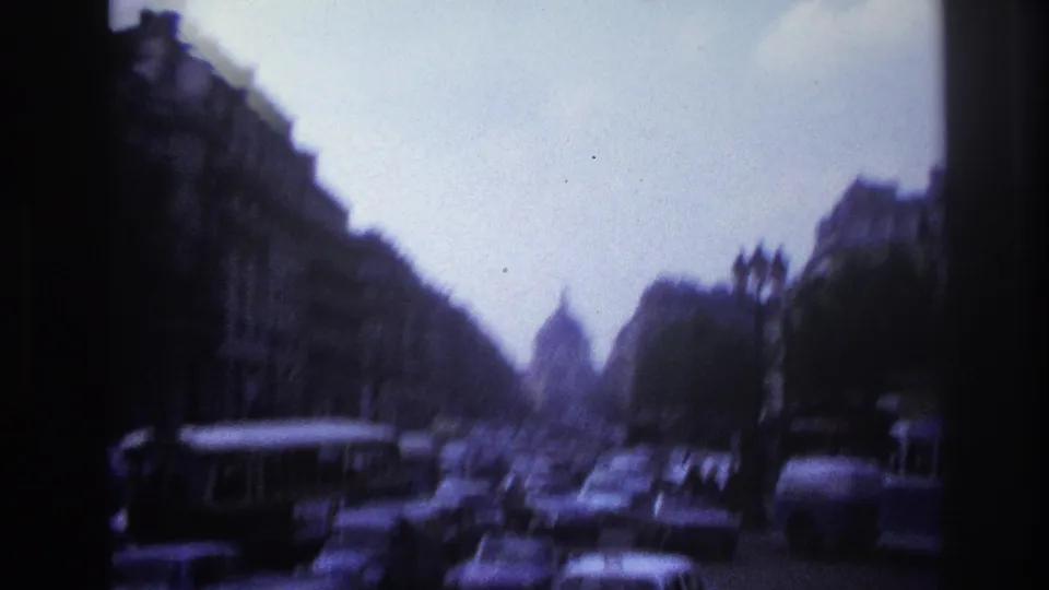 1967 Paris moving-vehicle view looking down a busy street with buses, cars, trees, and a distant domed building shape.