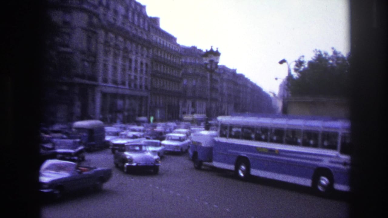 Cars and a blue-and-white bus pass along a broad city street beside large buildings.