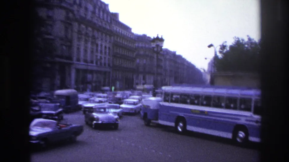 1967 Paris street scene with classic cars, a blue-and-white bus, boulevard architecture, and tree-lined public space.
