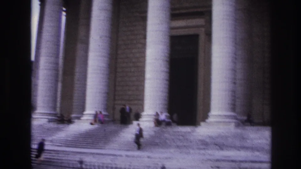 1967 Paris home-movie frame of pedestrians at the entrance steps of a large classical stone building with tall columns.