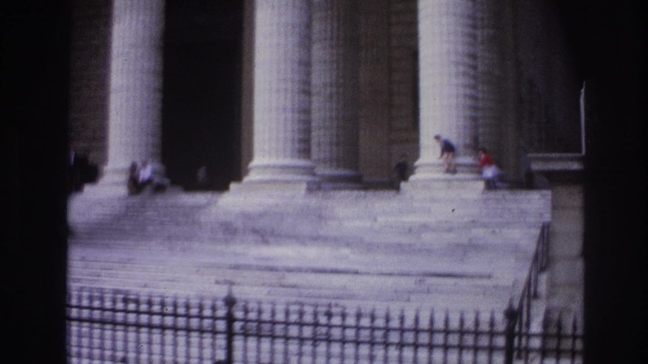 1967 Paris home-movie frame showing a classical colonnaded building, broad steps, iron fence, and small figures near the entrance.