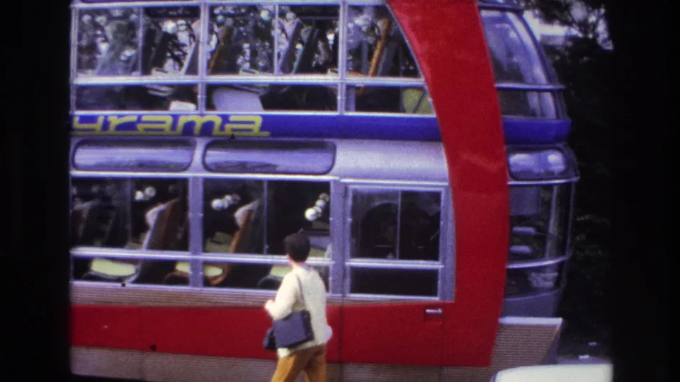 1967 Paris home-movie frame showing the Cityrama bus side windows and a woman in yellow pants carrying a dark handbag.