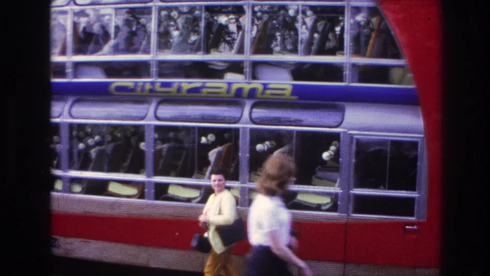 1967 Paris frame with Cityrama bus windows, visible passengers, a woman near the bus, and a blurred pedestrian in the foreground.
