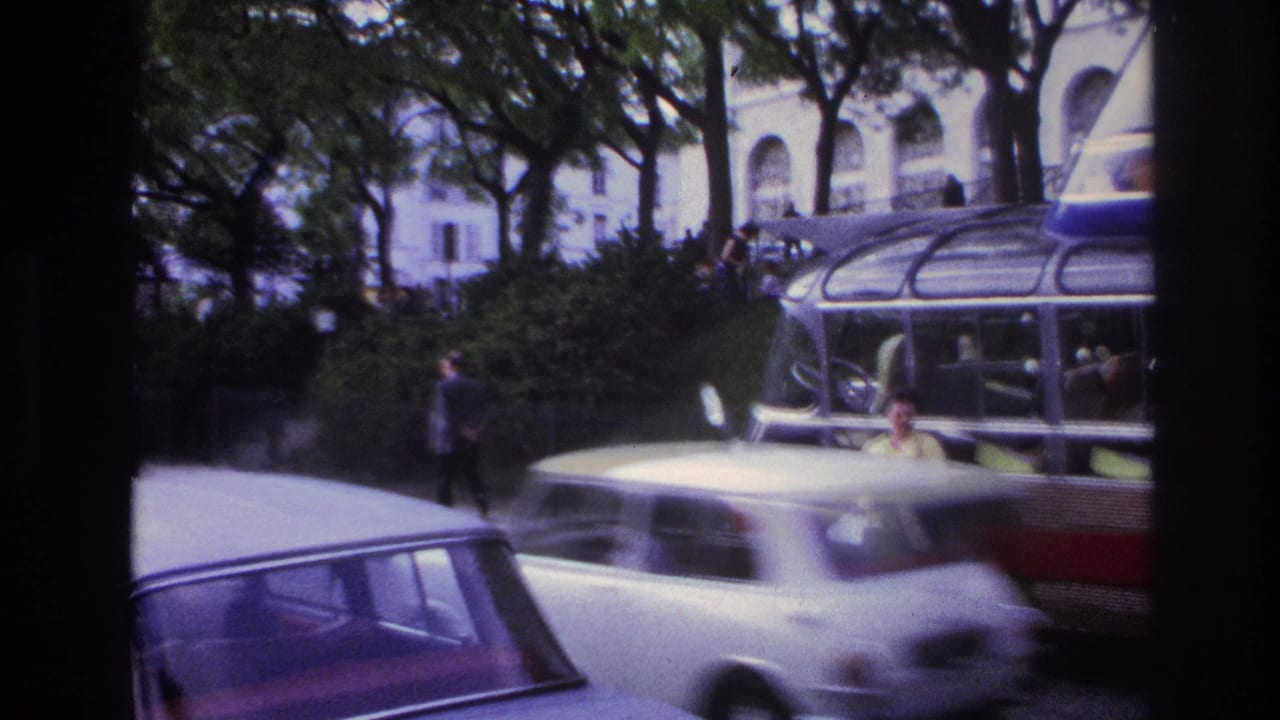 White car passes in front of the sightseeing bus while the woman stands near the curb.