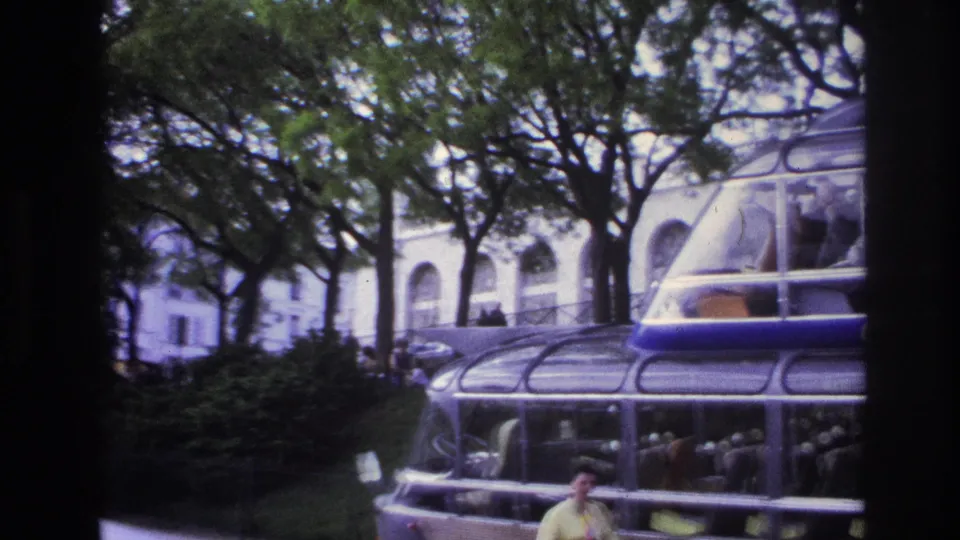 Final 1967 Paris frame with the red and silver sightseeing bus prominent, trees overhead, and the posing woman partly visible near the lower edge.