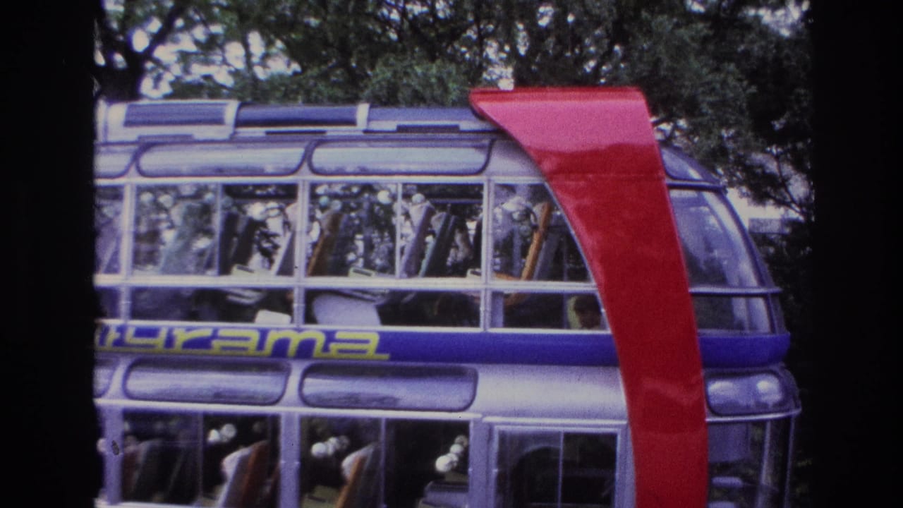 1967 Paris 8mm frame showing a glass-sided modern structure, red curved support, trees, and partial signage behind dark foreground bars.