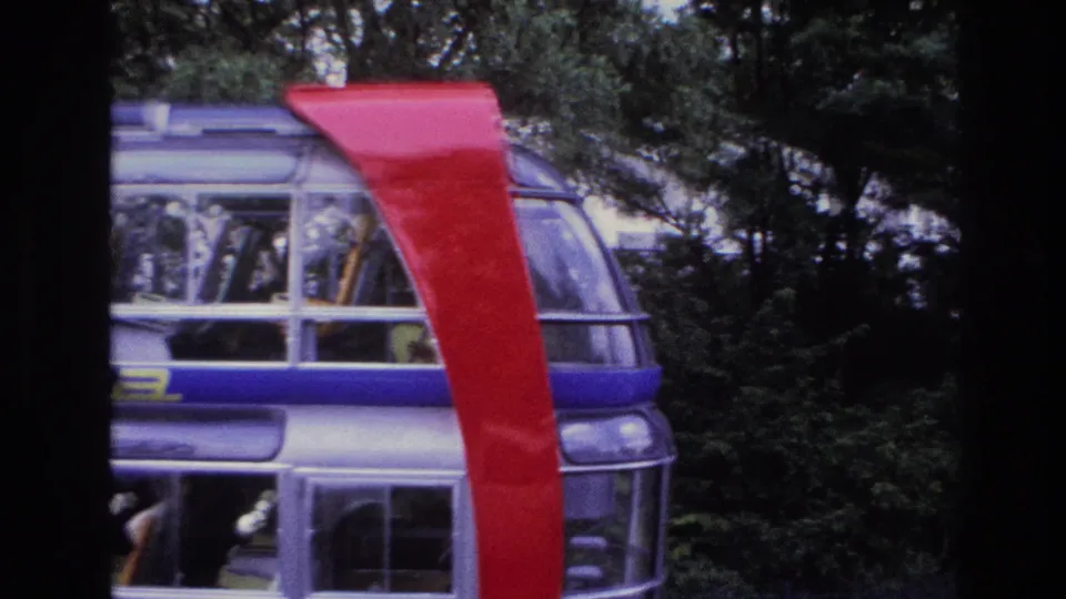 1967 Paris 8mm frame with a glass-sided structure, red curved support, blue stripe, partial lettering, and wooded background.