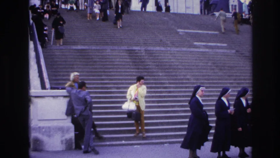 1967 Paris 8mm frame showing nuns in traditional habits, tourists, a woman in a yellow jacket, and people on broad stone steps.