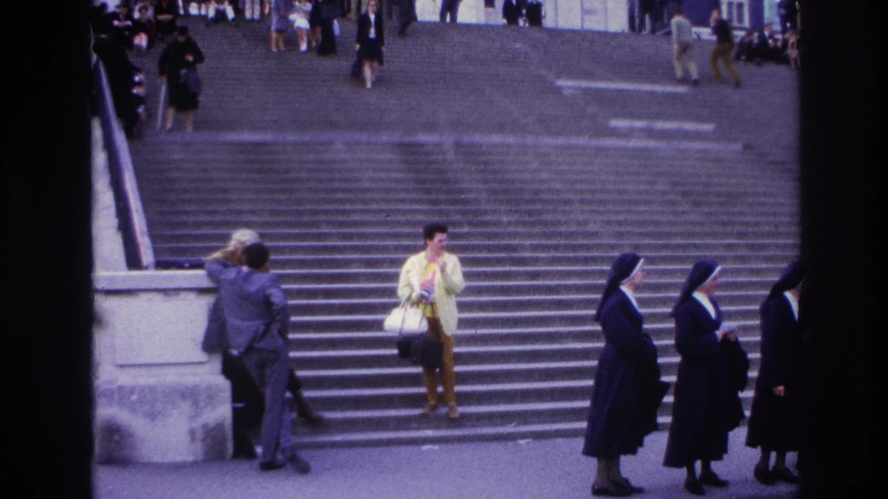 1967 Paris home-movie frame showing people on wide steps, including nuns in dark habits and a woman in a yellow jacket.