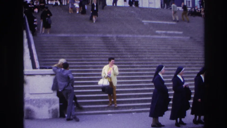1967 Paris home-movie frame showing people on wide steps, including nuns in dark habits and a woman in a yellow jacket.