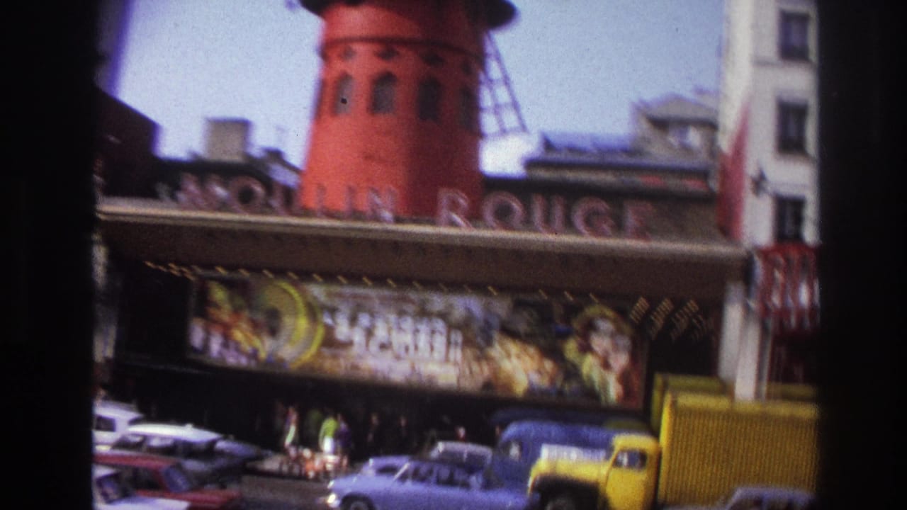 Moulin Rouge windmill and marquee with classic cars and a yellow vehicle at street level.
