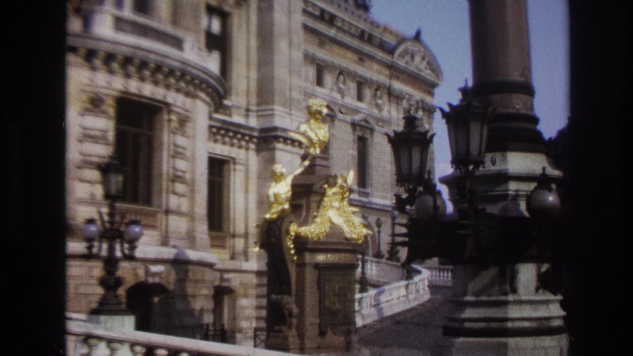 1967 Paris home-movie frame showing a grand stone facade with gilded sculpture, dark lampposts, and a curved balustrade.