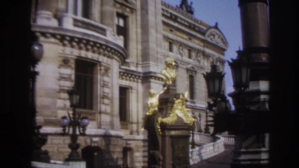 1967 Paris 8mm frame holding on gilded sculpture against an ornate stone building with lamps and a curved balustrade.