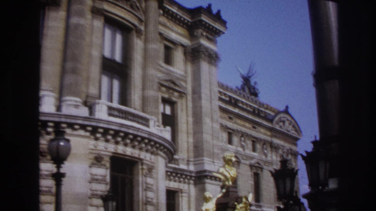1967 Paris home-movie frame showing a grand stone facade with gold sculptural figures, carved windows, and lamp posts.