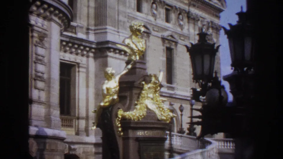 1967 Paris exterior frame with gilded sculpture, ornate stone windows, columns, balcony railings, and dark lamps in the foreground.