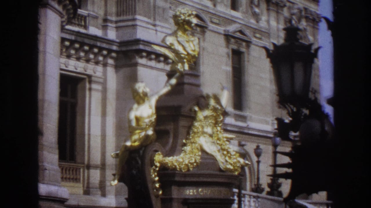 1967 Paris home-movie frame showing gilded sculptural figures on a grand stone building facade.