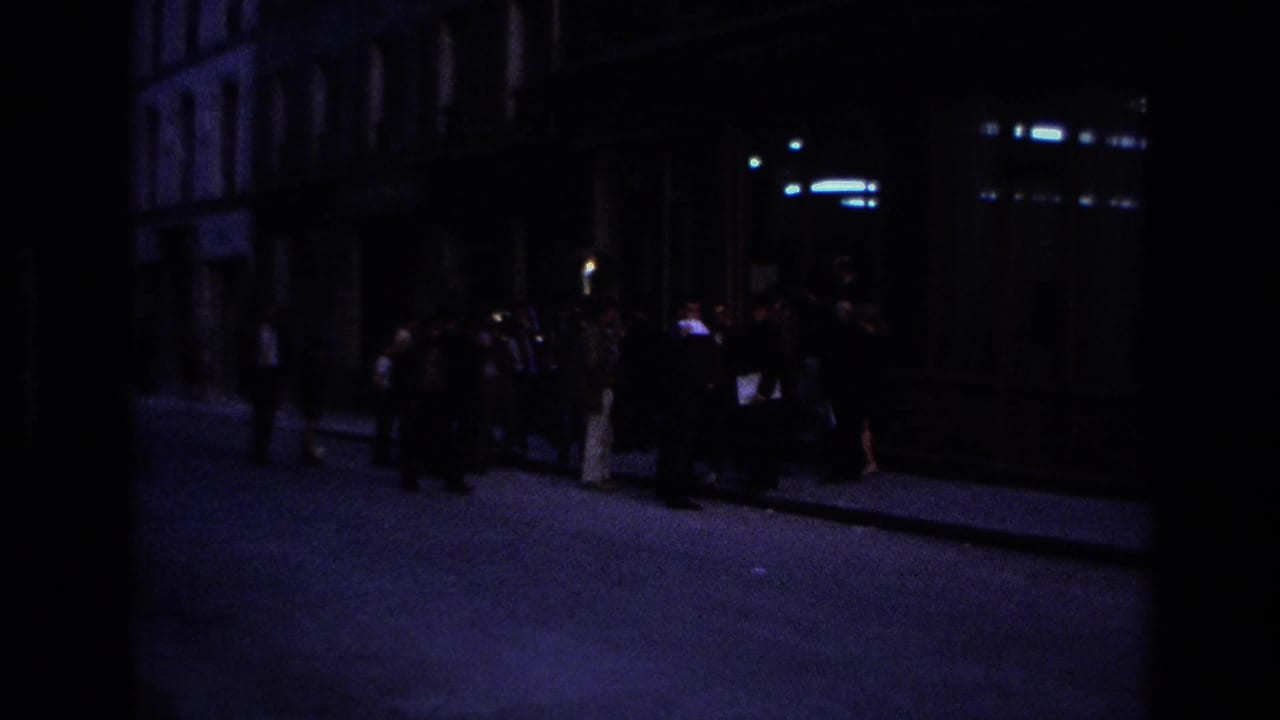 Nighttime 1967 Paris street view with a small group gathered on a dim sidewalk beside dark building fronts.