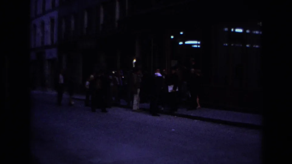 Nighttime 1967 Paris street view with a small group gathered on a dim sidewalk beside dark building fronts.