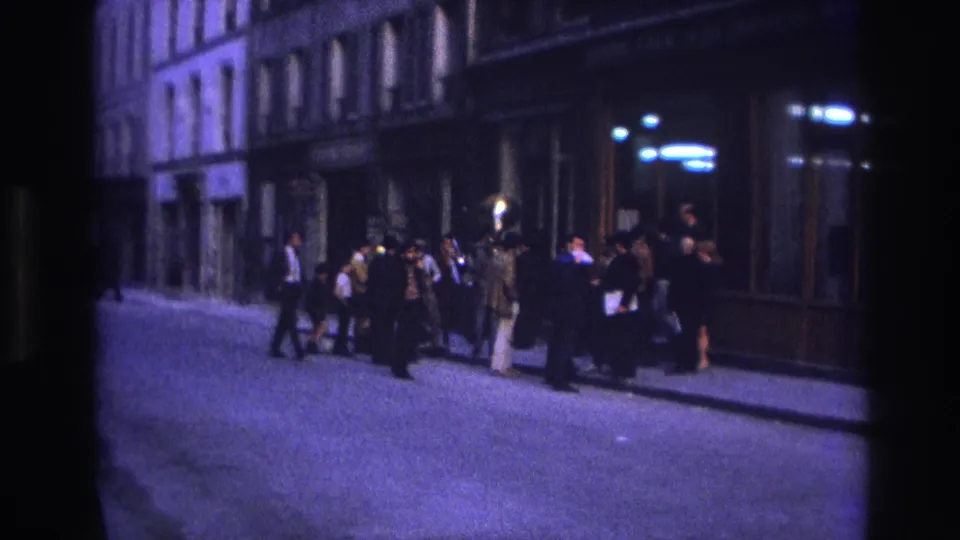 1967 Paris street frame showing pedestrians and a clustered sidewalk group under low nighttime light.