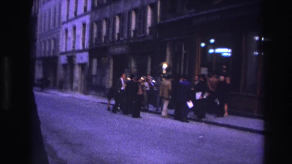 End frame of a 1967 Paris sidewalk gathering, with figures clustered near dark building fronts and street lighting.