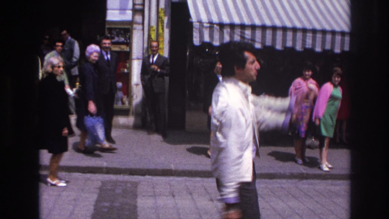 Man in a white jacket passes in front of pedestrians under a striped awning.