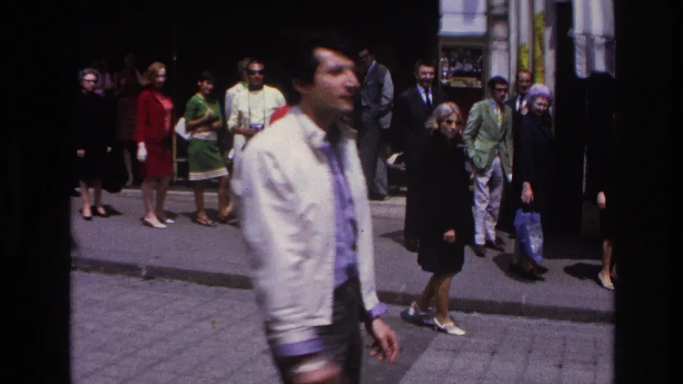 1967 Paris frame with a soft-focused man in a white jacket in the foreground and several adults watching from the sidewalk.