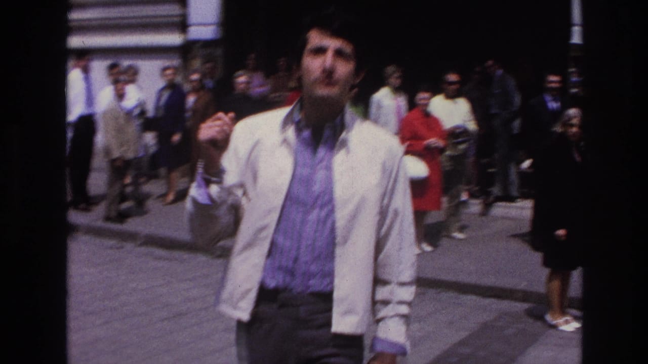 In Paris, 1967, a man in a white jacket and purple shirt gestures toward the camera as pedestrians move behind him.