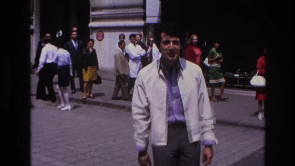 A 1967 Paris street frame shows the man nearer to camera, with passersby, cobblestones, and a stone facade visible behind him.