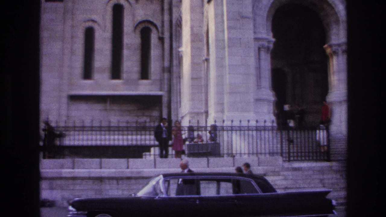 Dark sedan in front of a stone church facade with railings and people near the steps.