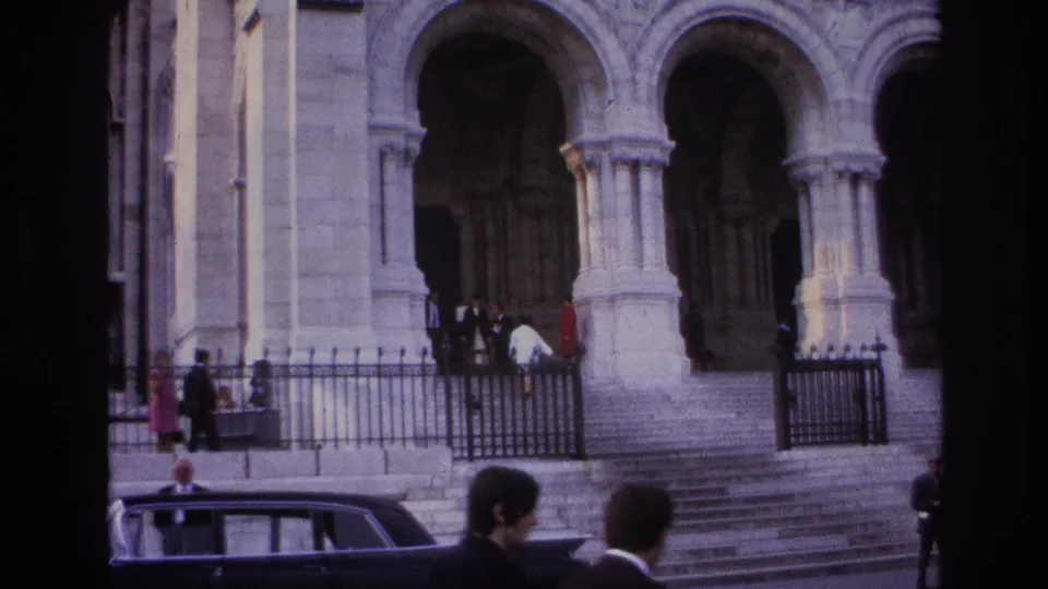 1967 Paris frame showing arched stone portals, broad steps, people near the entrance and railings, and a dark sedan in the foreground.