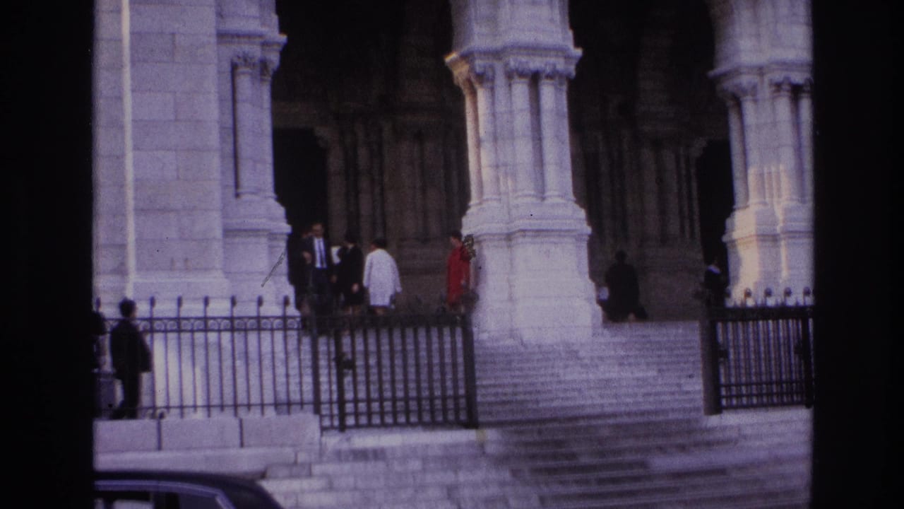 Pedestrians stand and walk near arched stone entryways behind black iron railings.