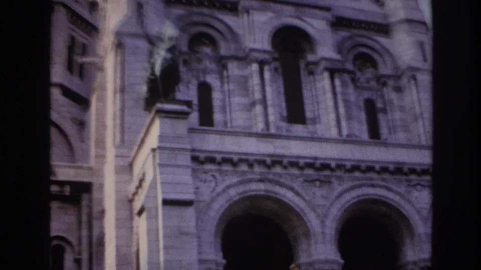 1967 Paris home-movie frame showing the building facade with arched windows, large stone portals, columns, and soft faded color.