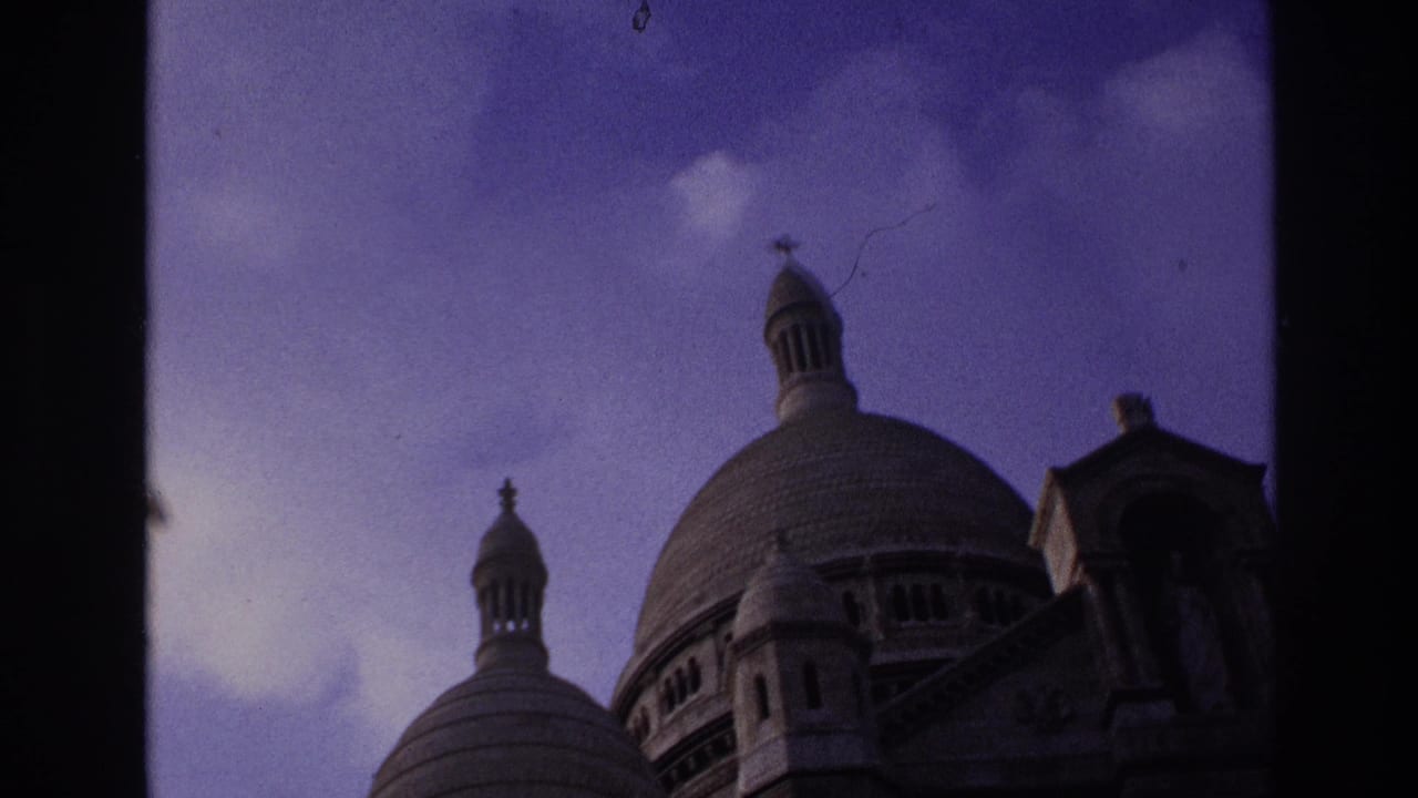 1967 Paris home-movie frame showing Sacre-Coeur domes and cupolas partially bordered by a dark window frame.