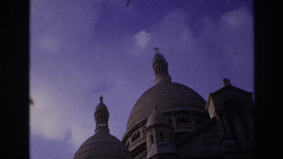 1967 Paris home-movie frame showing Sacre-Coeur domes and cupolas partially bordered by a dark window frame.