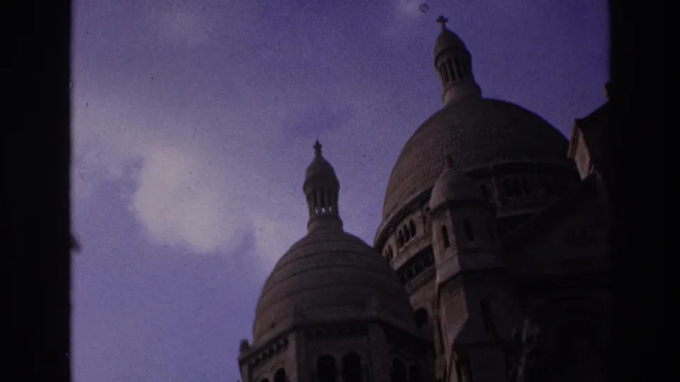 1967 Paris frame with Sacre-Coeur Basilica domes, arched openings, and dark building edges against a cloudy purple sky.