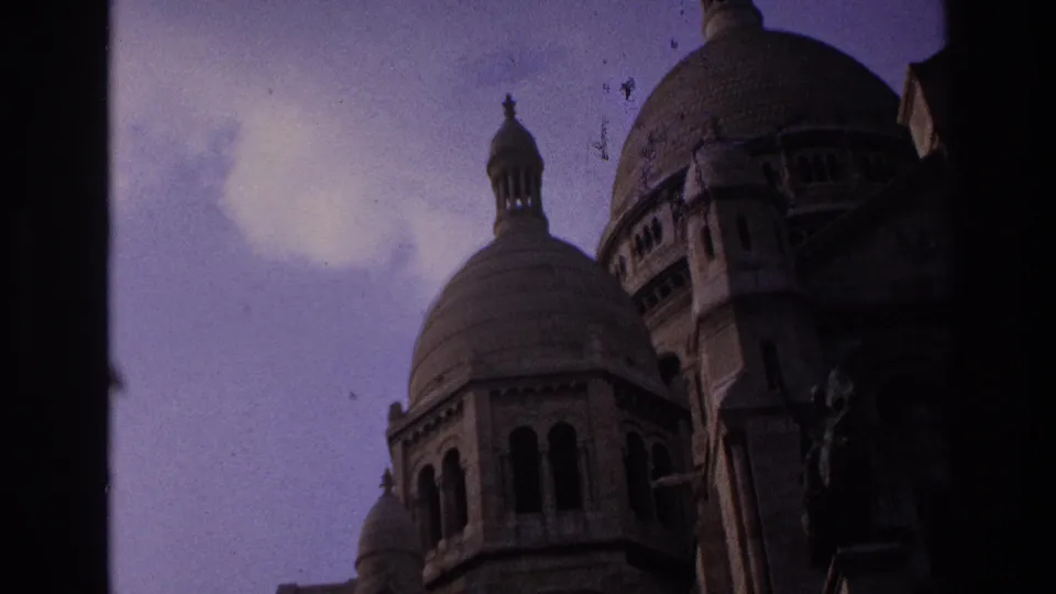 1967 Paris home-movie frame showing a closer low-angle view of Sacre-Coeur stone domes with visible film specks.