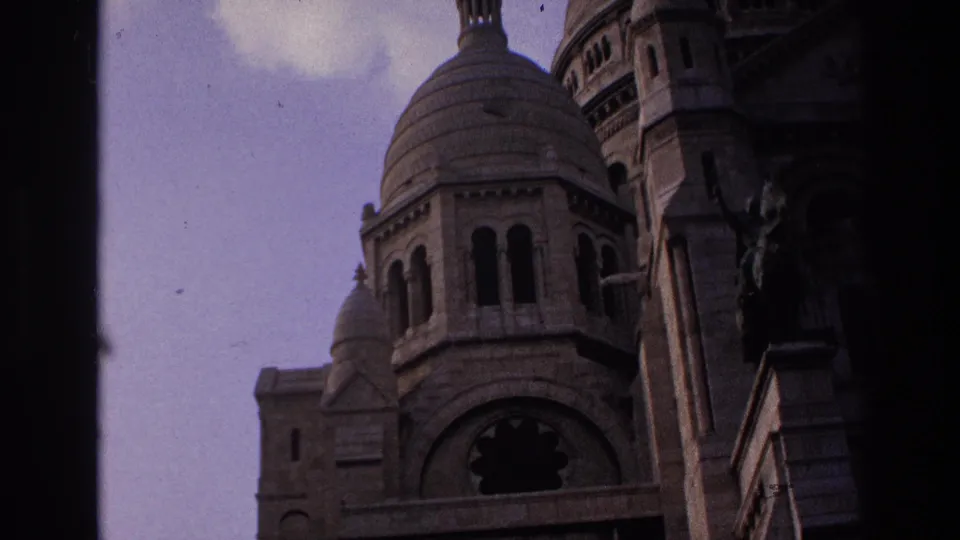 1967 Paris 8mm frame showing Sacre-Coeur's dome, arched openings, pale sky, and heavy dark vignette from the film frame.