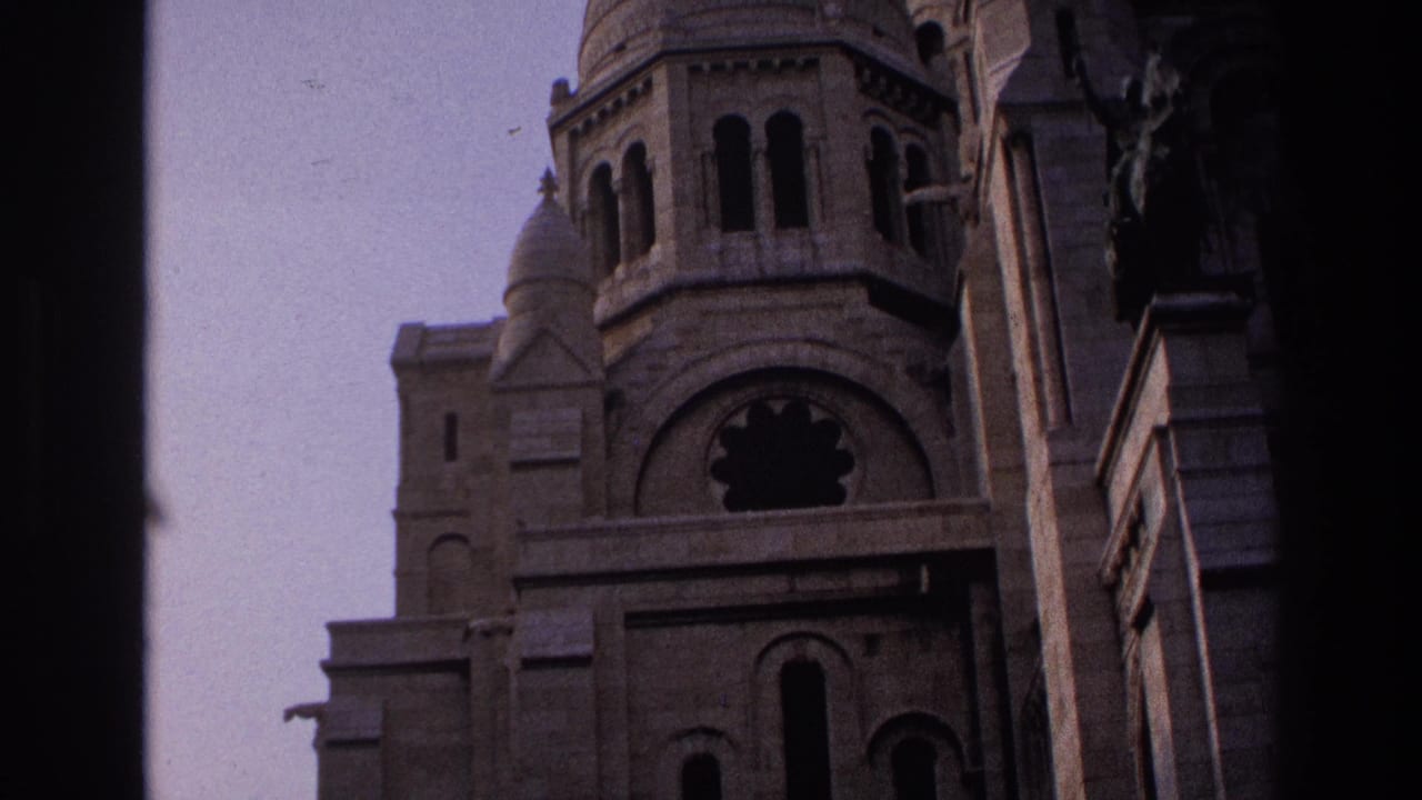 Stone tower and arched facade of Sacre-Coeur framed by dark vertical film edges.