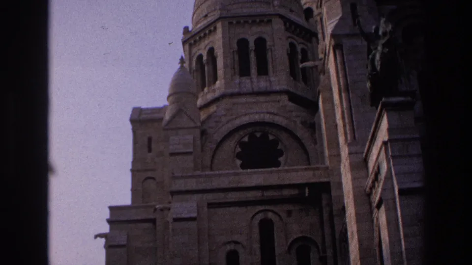 1967 Paris view of Sacre-Coeur's tower, rounded arches, stonework, and neighboring building edge within a dark 8mm frame.