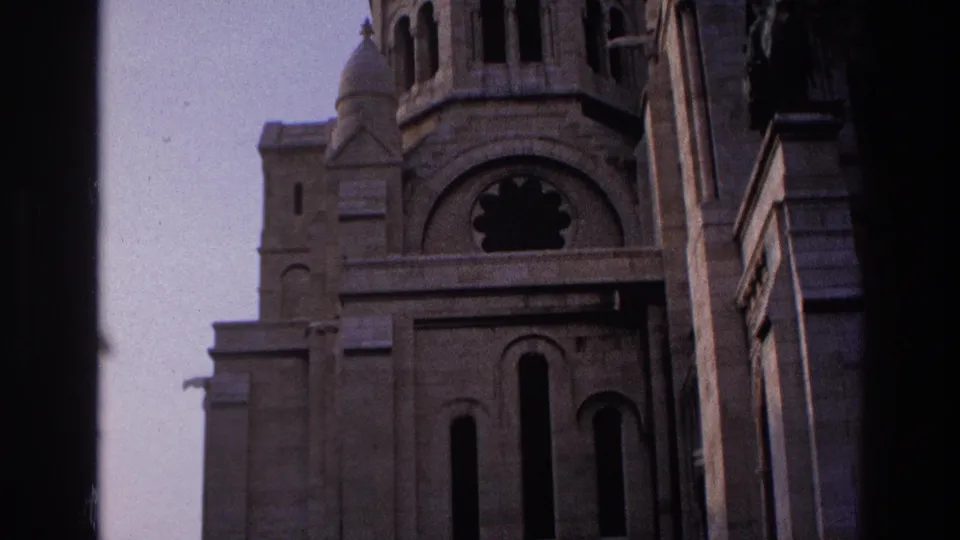 1967 Paris 8mm frame looking up at Sacre-Coeur's facade, with the dome partly visible and a dark vertical film border at right.