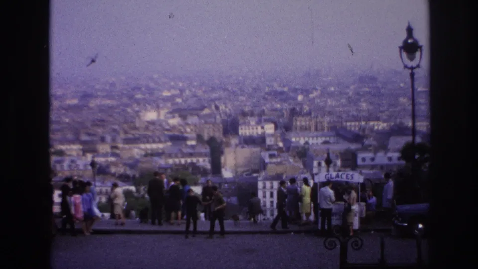 A wide 1967 Paris overlook view shows visitors standing near the edge as birds pass over the hazy city skyline.